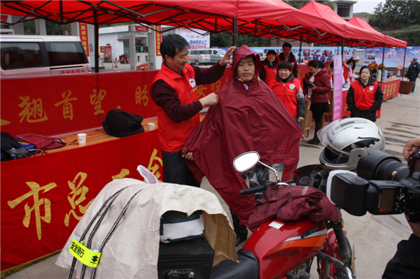 梧州市總工會的黨員義工們在市東出口春運服務(wù)站助力“摩托大軍”平安返鄉(xiāng)，幫助他們檢查車輛和行李，穿上雨衣。--黃賀峰攝.j